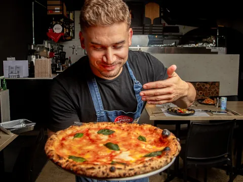 A pizzaiolo in an apron holding out a margherita in the dining room
