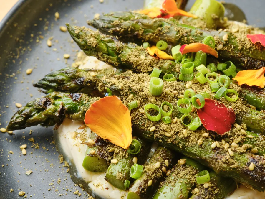 Charred asparagus over a white pur&eacute;e with a green crumb and edible petals