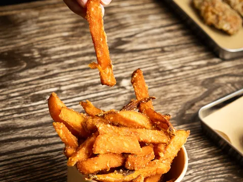 A sweet potato fry lifted out of a branded paper cup