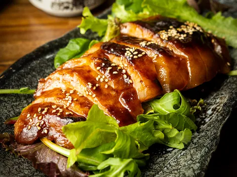 A glazed, sesame-topped grilled fillet on a stone plate with salad leaves