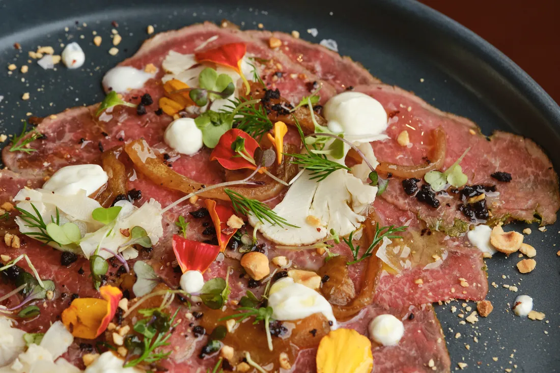 Beef carpaccio dotted with cream, herbs and edible flowers, from above
