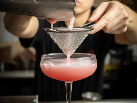 A pink cocktail strained into a coupe at the bar