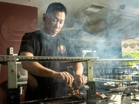 A chef working skewers over a smoking charcoal grill