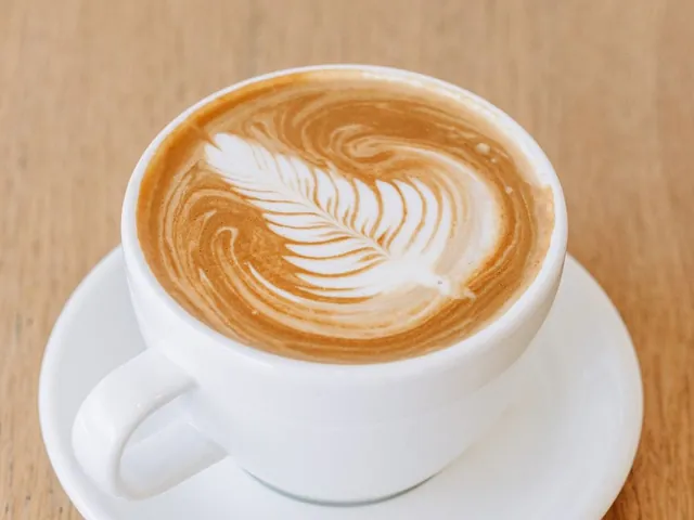 A flat white with latte art on a timber bench