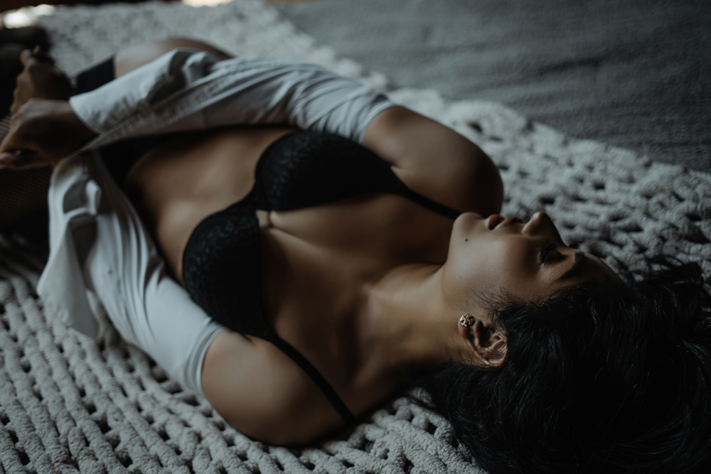 Woman with long hair laying on a knit blanket, wearing a white button-down shirt and black bra