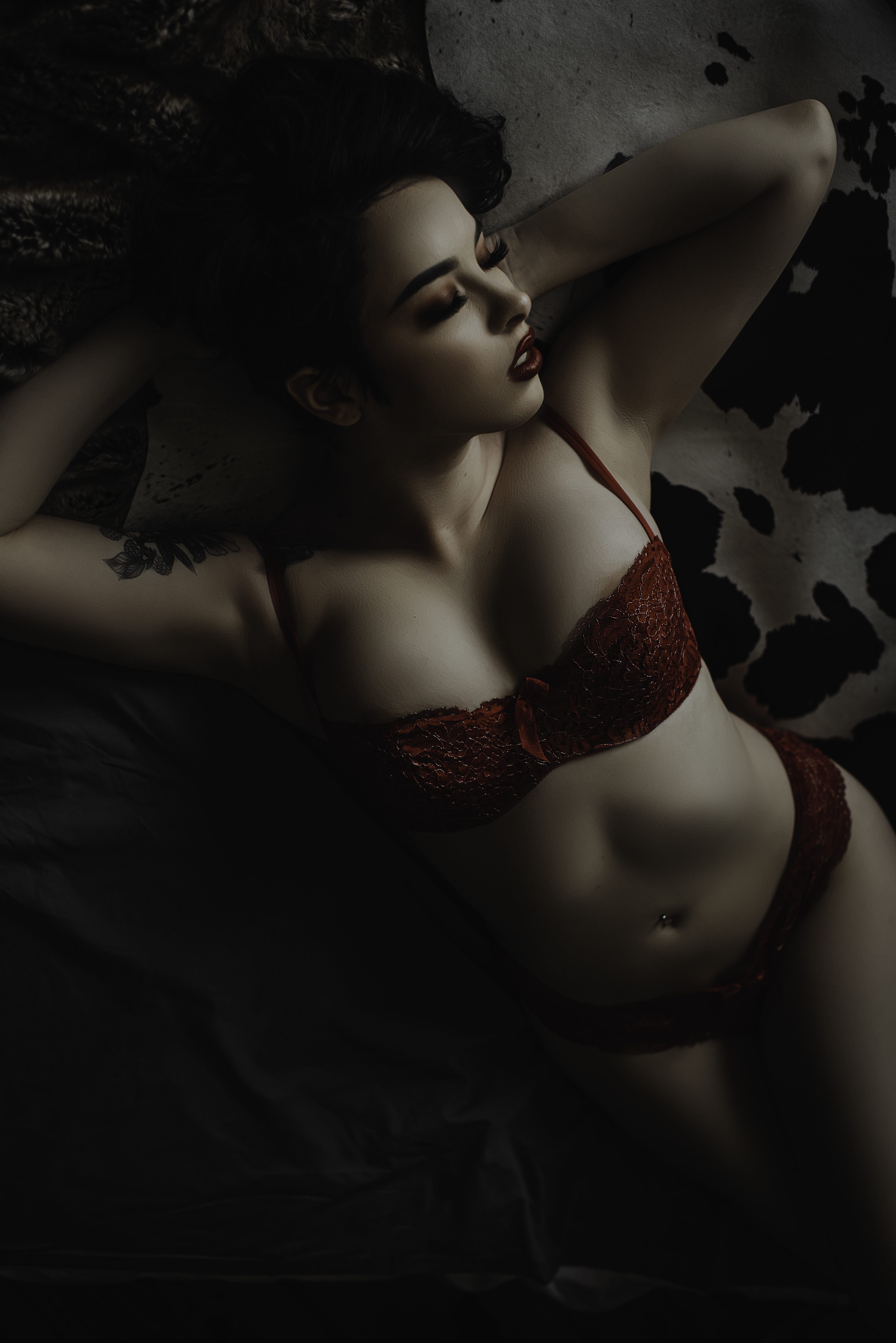 Woman with short hair laying on a cow rug wearing a red lingerie outfit