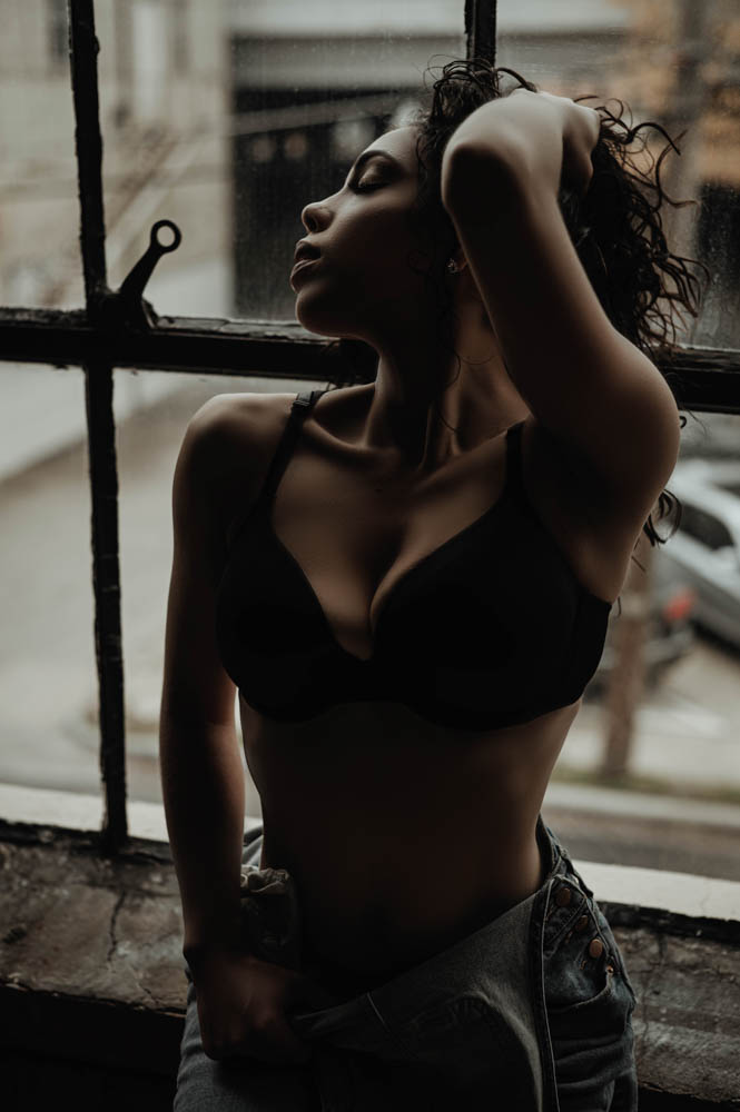 Woman sitting in window with denim jeans and a bra on