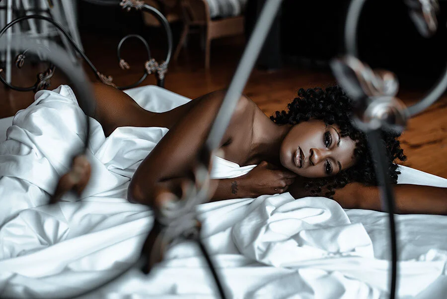 Black woman laying on antique style bed, wrapped in white sheets
