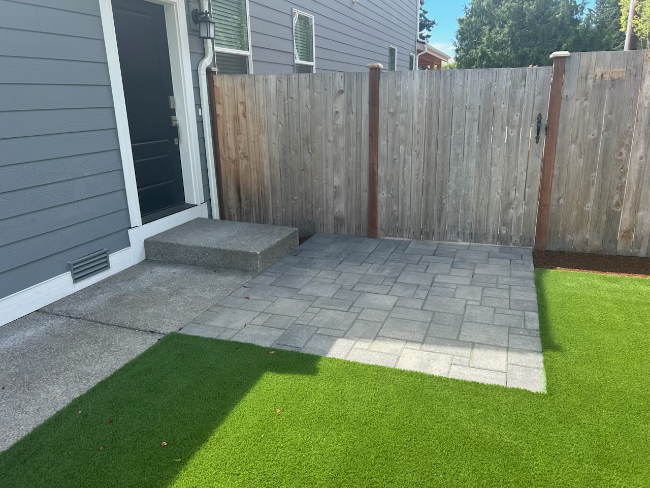Gray paver landing and green turf beside a back door and wood fence