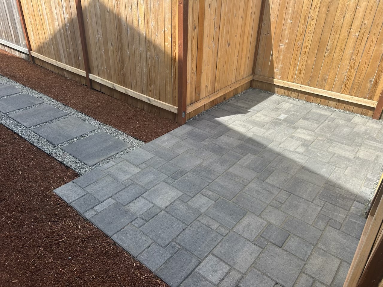 Gray paver patio joining a stepping-stone path beside a wood fence