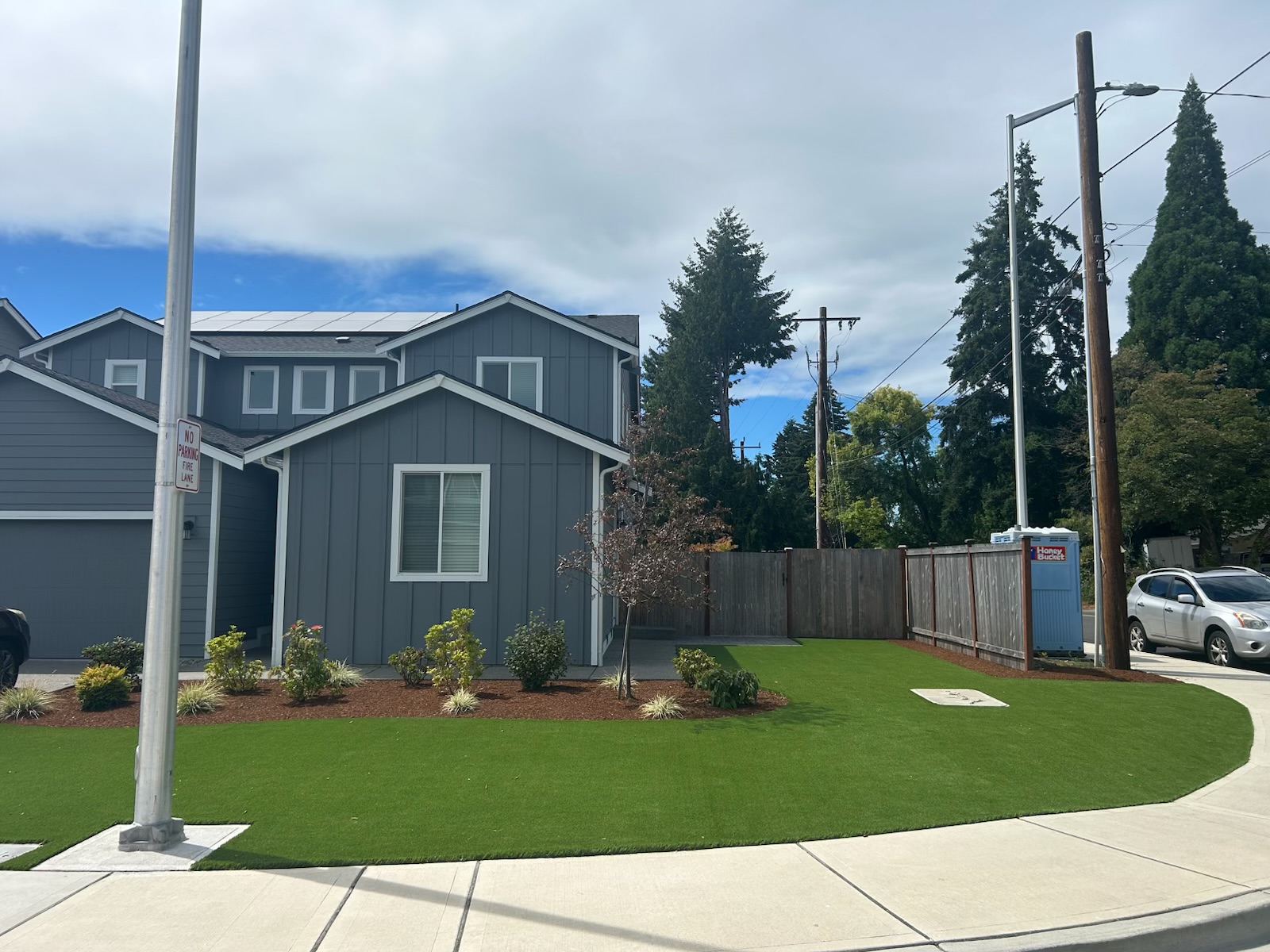 Green turf and mulched planting beds beside a gray house and curved sidewalk