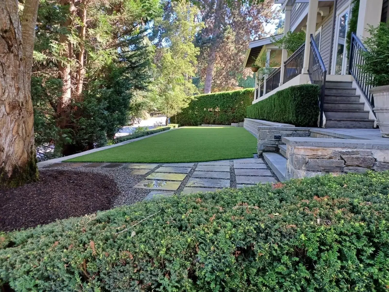 Front yard turf with stone steps, retaining walls, and trimmed hedges