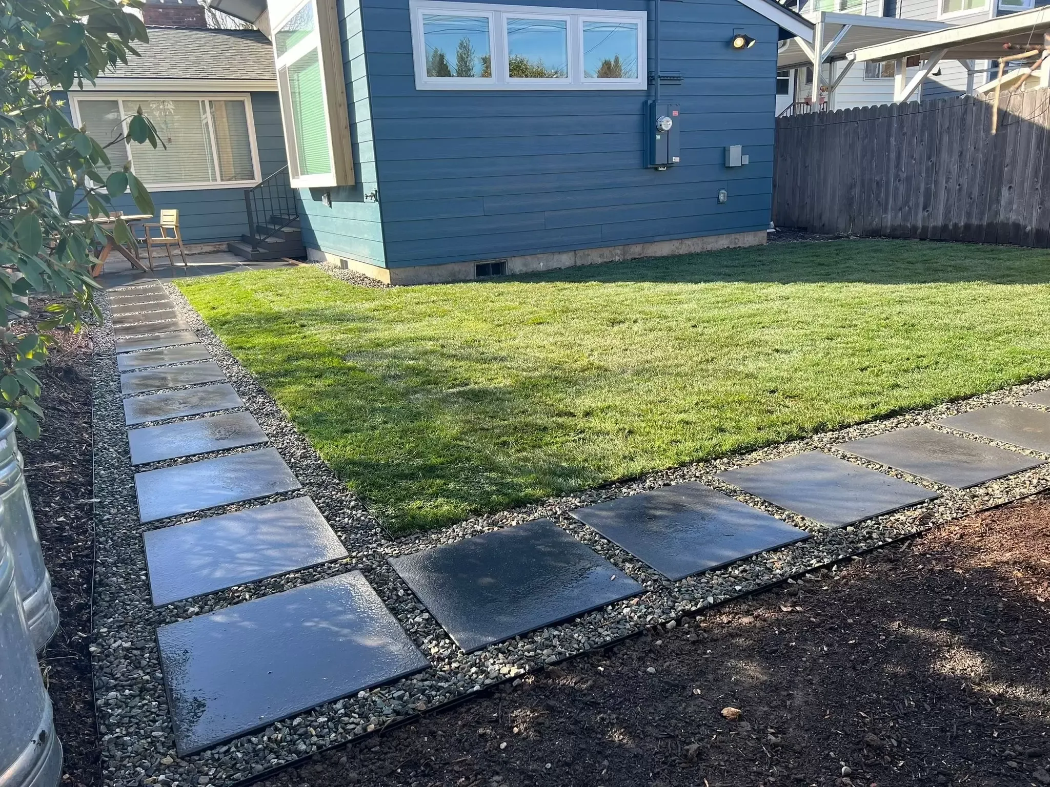 Green lawn bordered by rectangular pavers and gravel beside a blue house