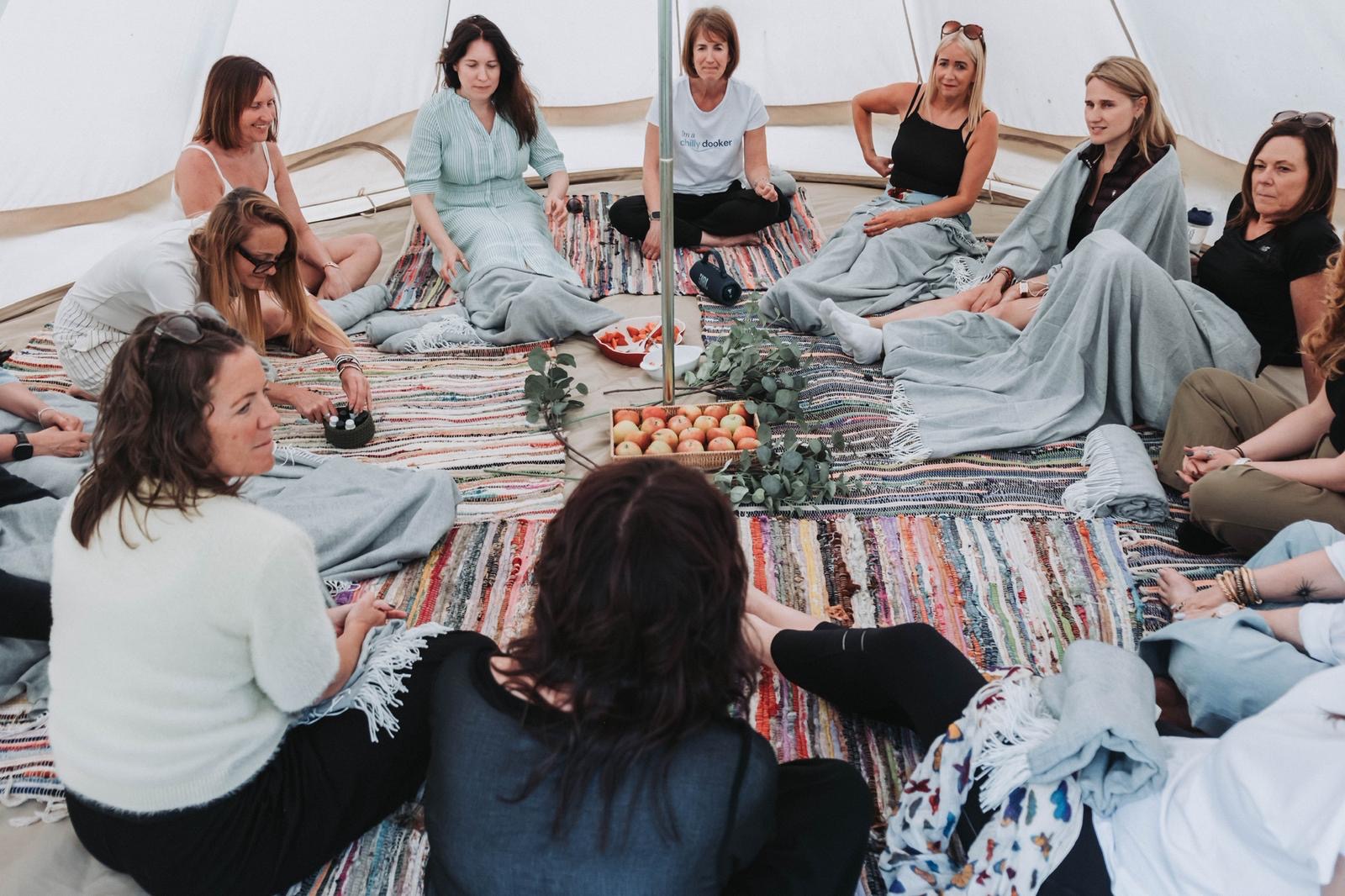 Group of women sitting in a circle in a bell tent, wrapped in blankets