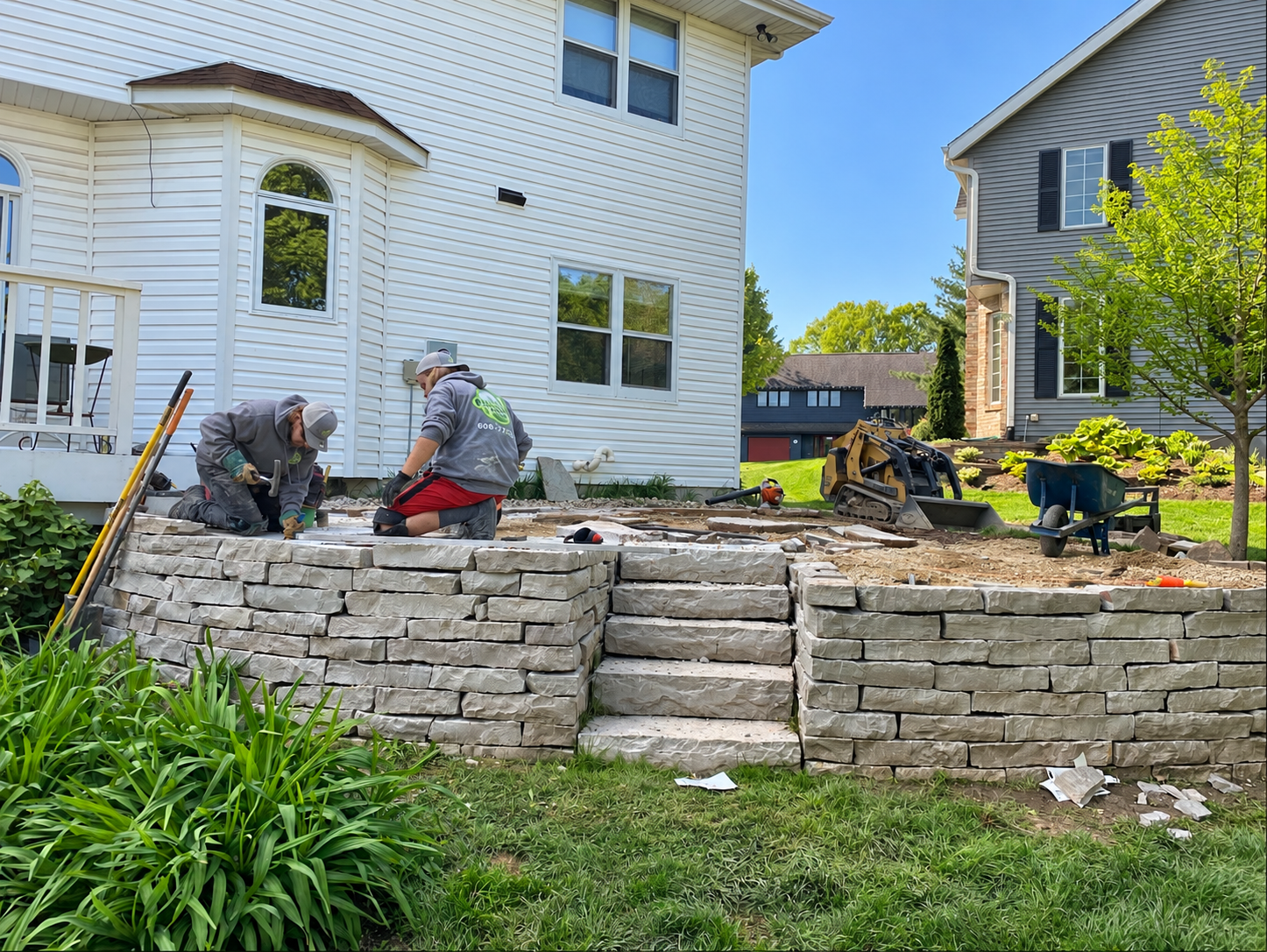 Paver patio with a curved block seat wall and Adirondack chairs beside a screened porch, with a stepping-stone path through a mulched bed.