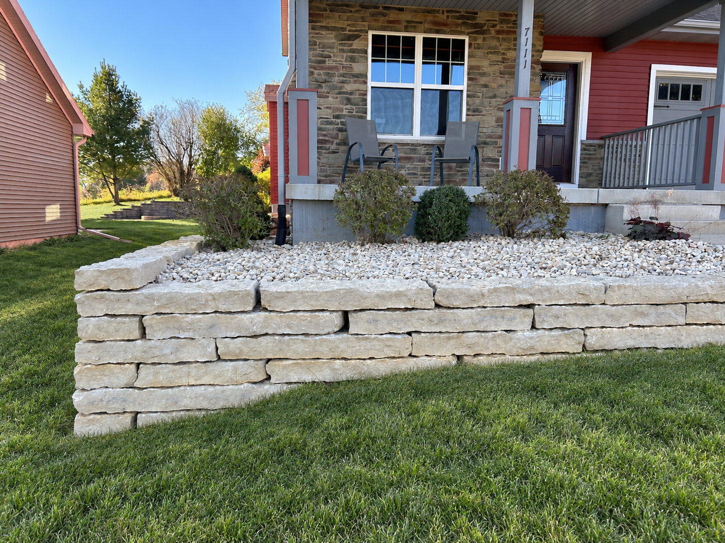Coursed stone retaining wall holding a raised front lawn and foundation plantings, stepping down as it follows the grade.