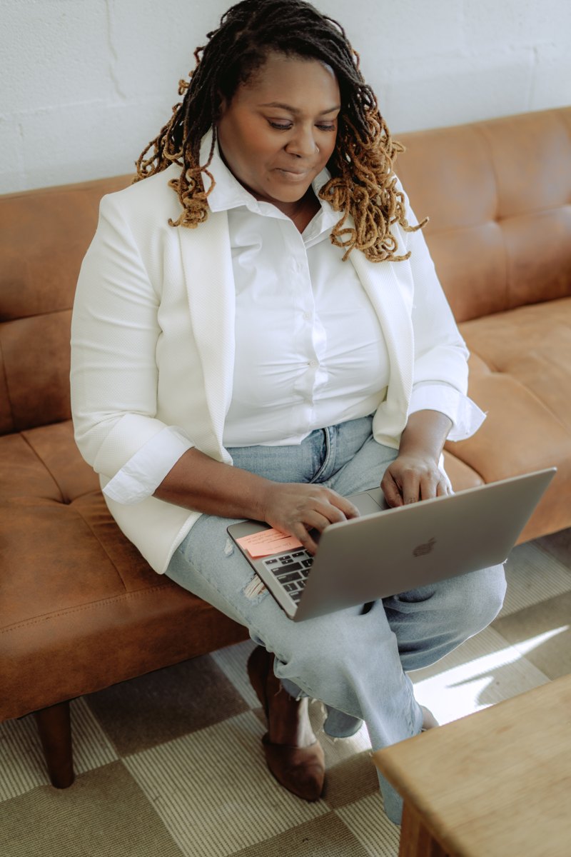 Starr Clinton smiling while working on her laptop on a leather couch
