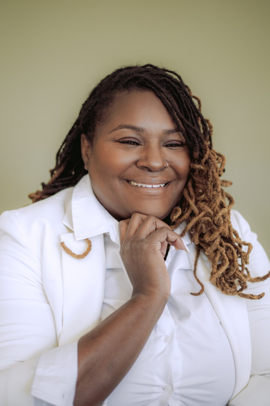Starr Clinton smiling in a white blazer against an olive background