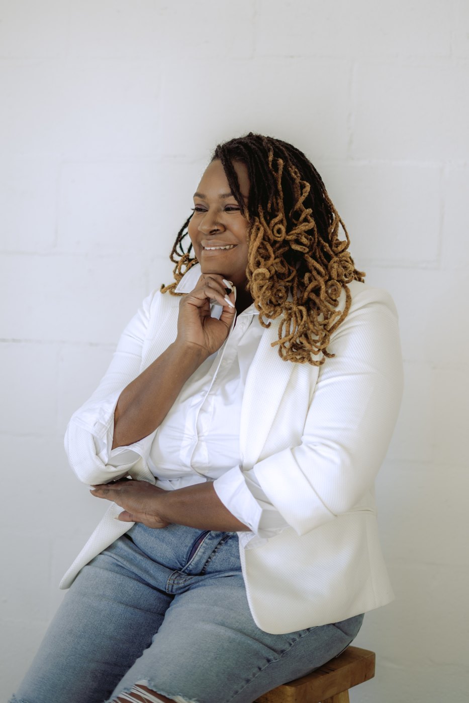 Starr Clinton smiling with her hand on her chin in a white shirt against a white brick wall
