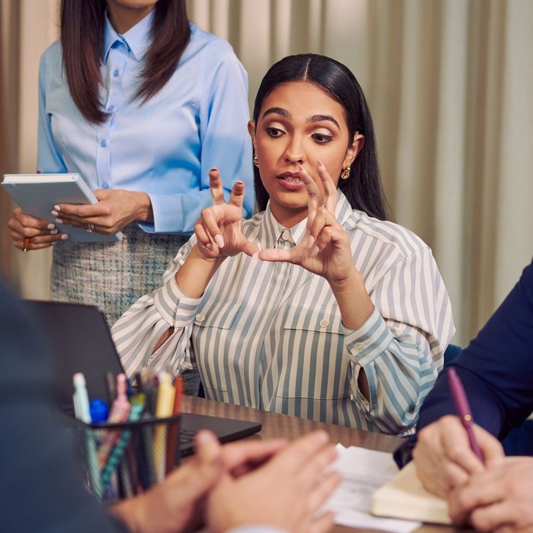 A Deaf professional signing to colleagues during a workplace meeting at a conference table