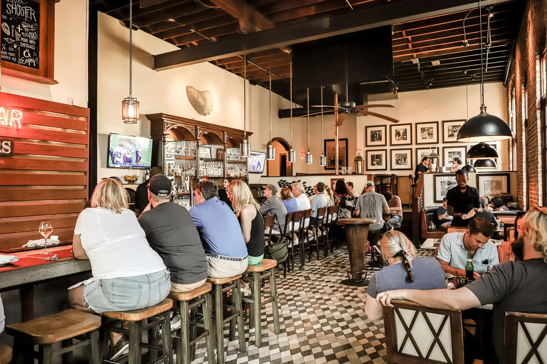 Guests dining and enjoying drinks at the bustling Oyster House bar and restaurant with televisions and framed art in a cozy, lively setting.