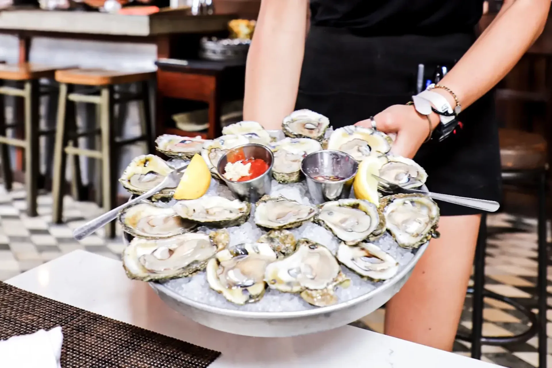 Server presenting a chilled oyster platter with lemon wedges and dipping sauces at Charleston Crab House.
