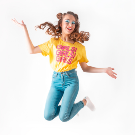 A tween or teen girl jumps up in celebration wearing a bright yellow shirt that reads, "Girls! Girls! Girls!"