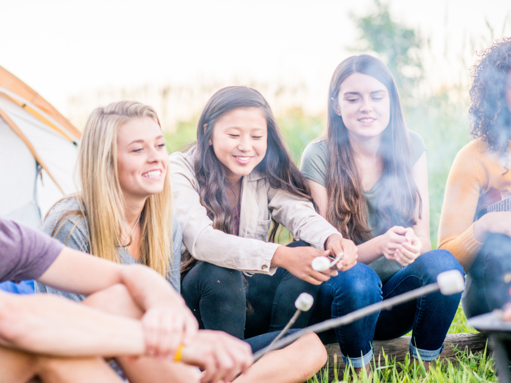 Teen and tween girl friends roast marshmallows over a campfire.