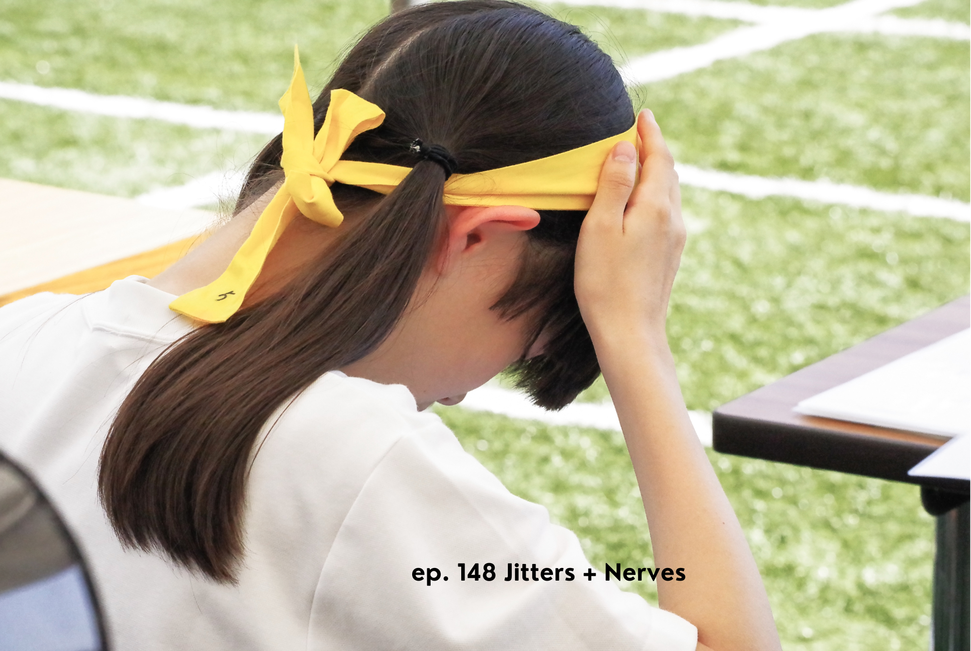 A tween or teen girl with a black ponytail sits on a soccer field sideline feeling jitters and nerves.