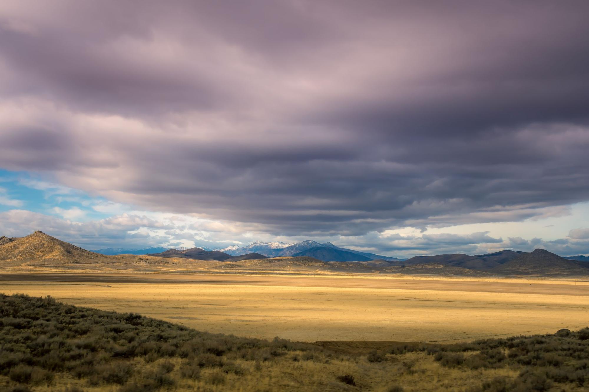 Storm clouds over a wide high-desert basin and distant ridgelines