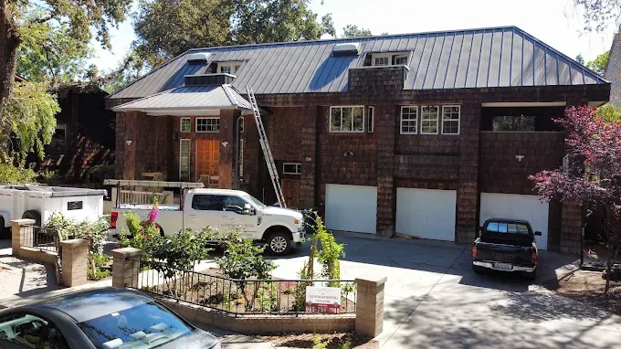 Recently installed roof vent on a suburban home with textured shingles, gutter system, blue sky, and greenery in Modesto California