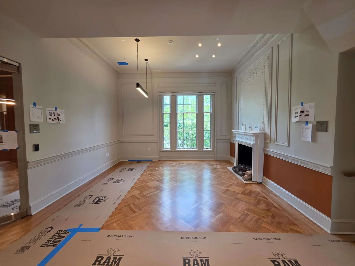 Empty grand room with parquet wood floor, fireplace, large windows, decorative molding, and modern pendant lights.