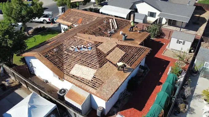Freshly repaired hail damage roof with clean shingles, reflecting sunlight, surrounded by lush greenery and neighborhood houses in Modesto California