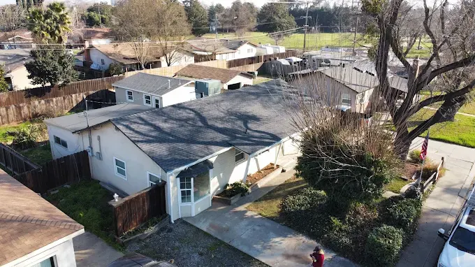 Close-up of dark gray asphalt shingles on a residential roof in Modesto CA with sunny sky and suburban neighborhood background