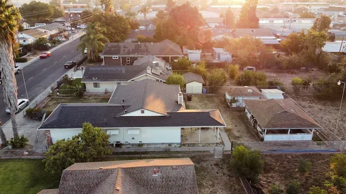 Restored asphalt shingle roof after hail damage in a suburban California neighborhood with lush lawns and clear sky