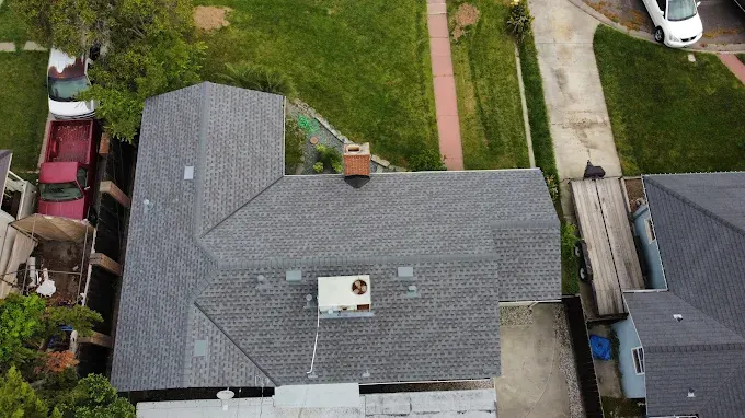 Freshly installed dark gray asphalt shingle roof on a modern home in Modesto California with lush lawns and blue sky