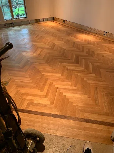 Gleaming hardwood floor installation in a minimalist Tice FL room with natural light and stylish decor elements.