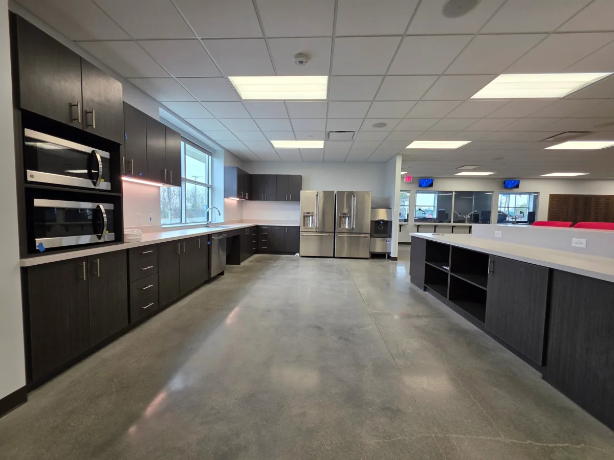 Expansive modern kitchen/breakroom with dark wood cabinets, stainless steel appliances, a long center island, and concrete floors.