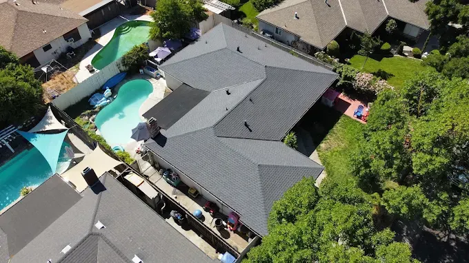 Close-up of a residential roof with new skylight flashing, asphalt shingles, and a bright suburban neighborhood background