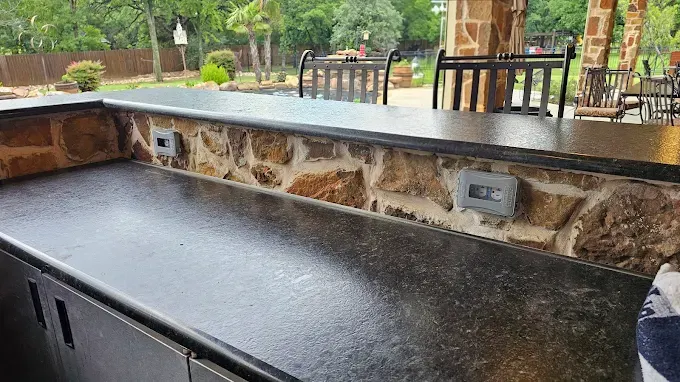 Outdoor electrical outlet on textured stucco wall with landscaped brick pathway and modern patio in Fort Worth TX