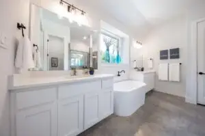Freestanding white bathtub with modern fixtures on marble floor in an elegant Austin Texas bathroom with natural light and greenery