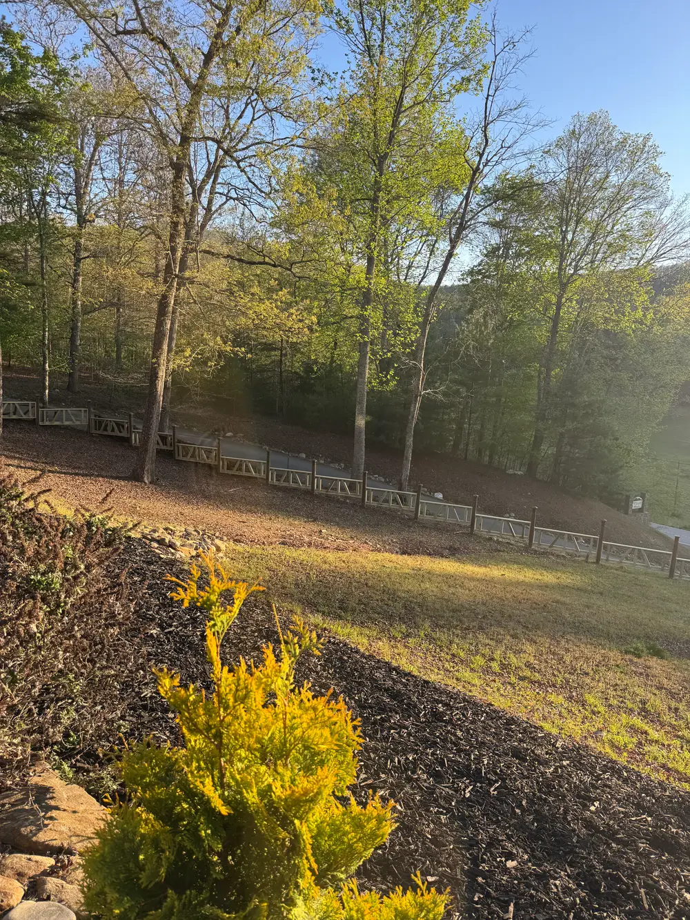 Beautiful wooden fence in White GA with natural finish, lush yard, flowers, and clear blue sky creating tranquility.