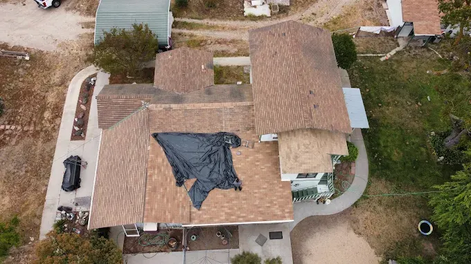 Newly completed roof replacement in Modesto CA showing modern grey asphalt shingles with lush landscaping and clear blue sky.