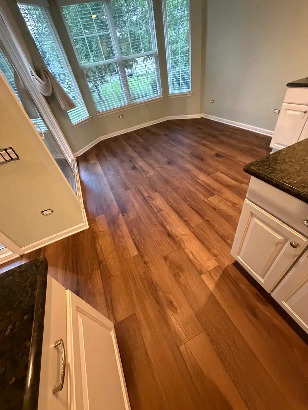 Bright kitchen/dining area features new wood flooring, light green walls, white cabinets, dark counters, and a bay window.