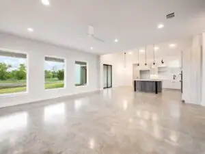 Modern Austin kitchen with white matte cabinets, warm wood accents, quartz countertops, stainless steel appliances, central island, natural wood flooring, recessed LED lighting, subway tile backsplash, large windows with greenery view, open shelving, and minimalist design.