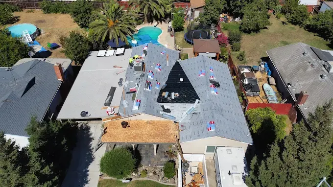 Completed gray shingle residential roof on modern suburban house in Modesto with lush lawn and neighborhood background