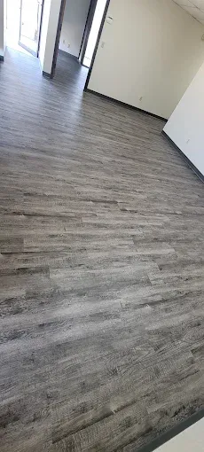 An empty room with new, light grey wood-look laminate flooring and white walls, featuring doorways in the background.