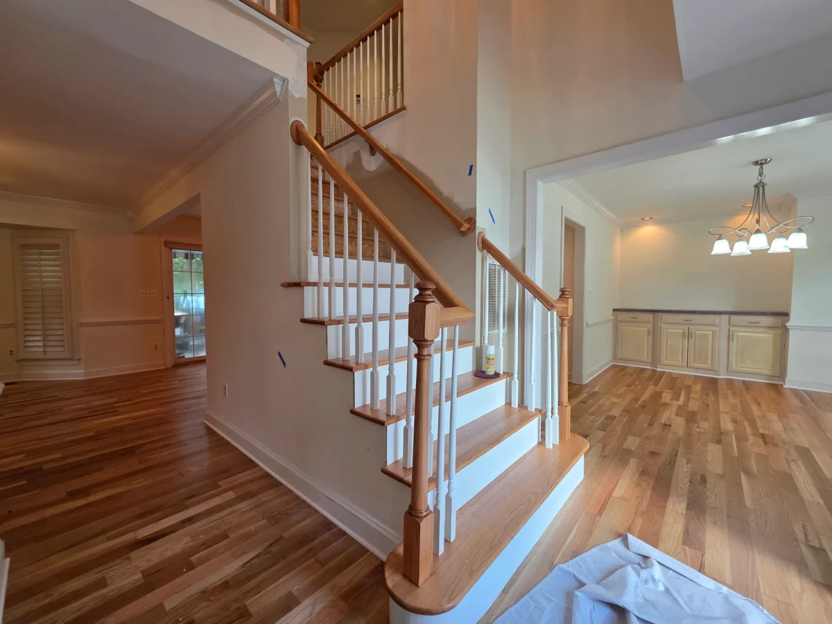 Renovated home interior with a wooden staircase, hardwood floors, and an open layout connecting bright living and dining areas.