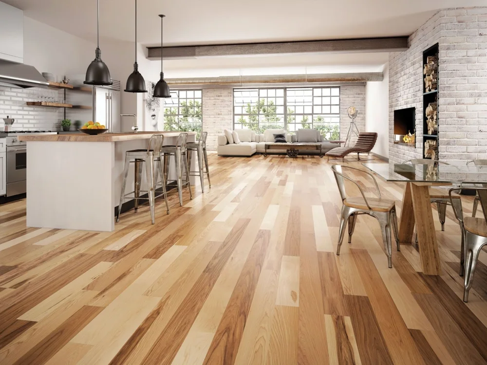 Modern industrial open-concept living space with a kitchen island, living room, dining area, brick fireplace, and hardwood floors.