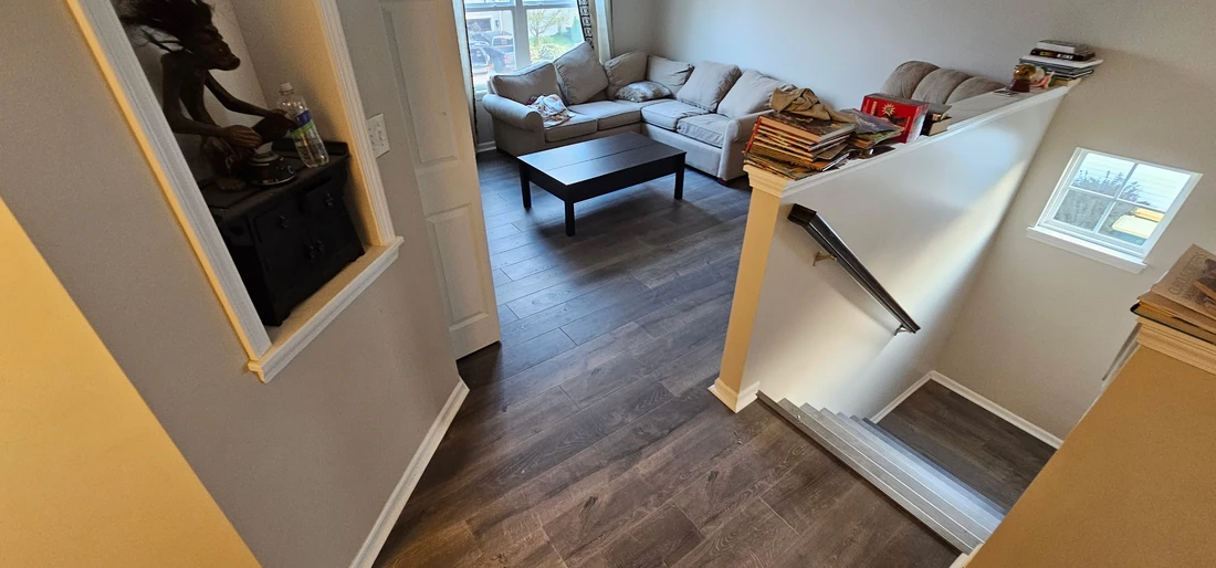 An elevated view of a cozy living room with a large sectional couch, coffee table, wood floors, and a descending staircase with books.